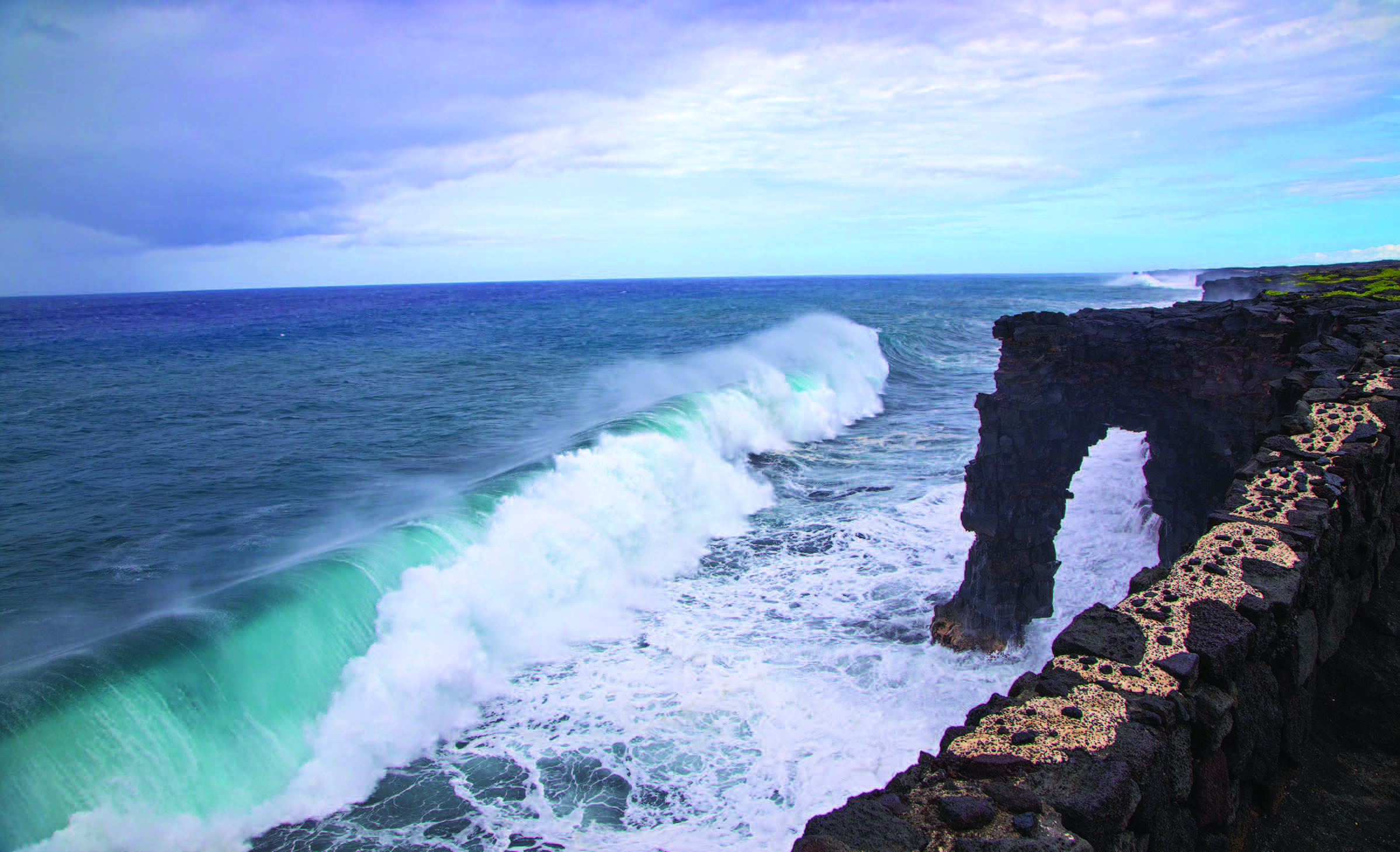 Rolling ocean wave crests near a natural rock arch at Hawai’i Volcanoes National Park