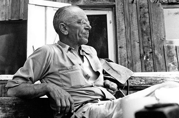 Aldo Leopold sitting in front of a cabin