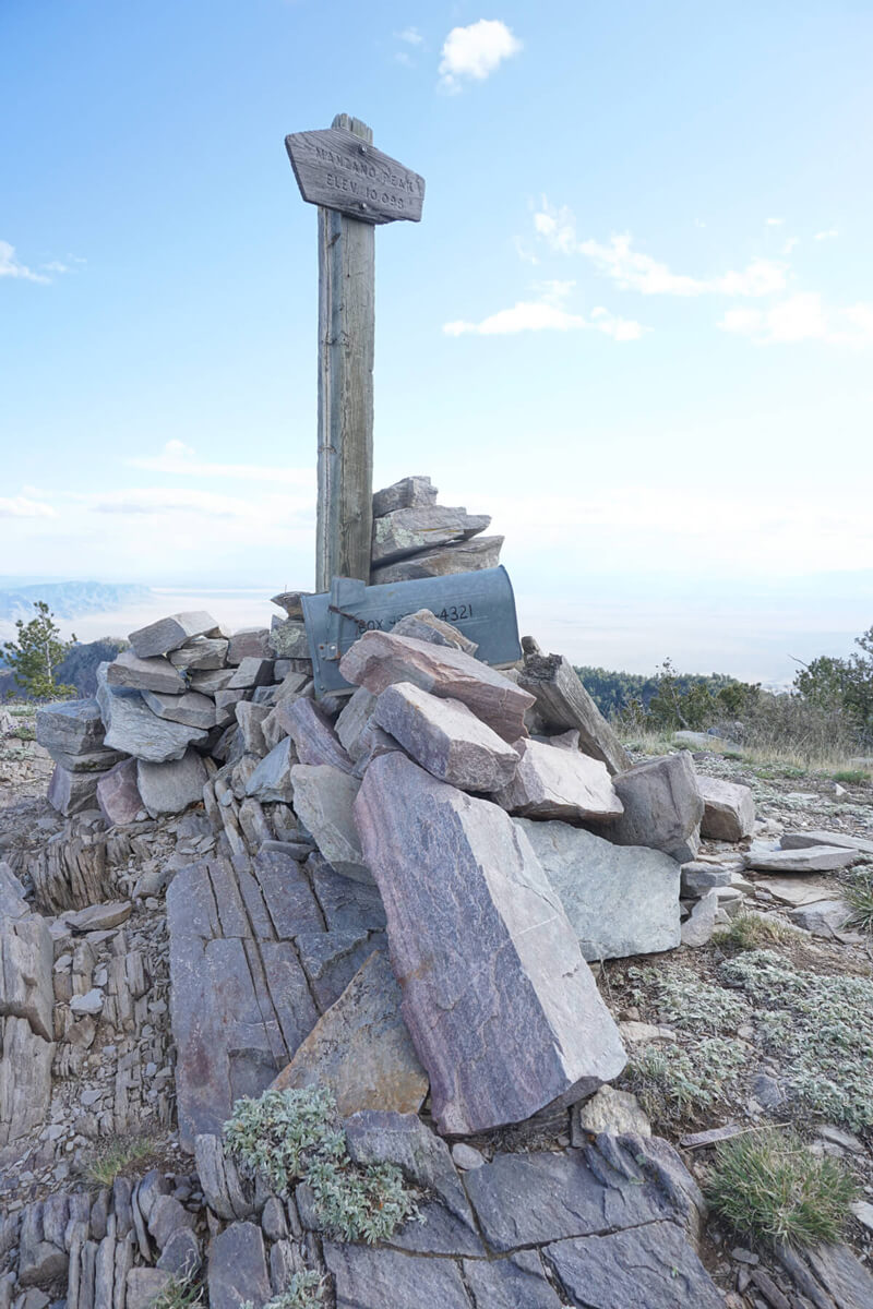 A sign displaying the name of a peak with a mailbox sticking out of the rocks