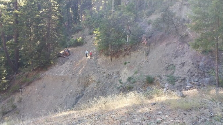 dirt road cut into the side of a hill with people walking in background