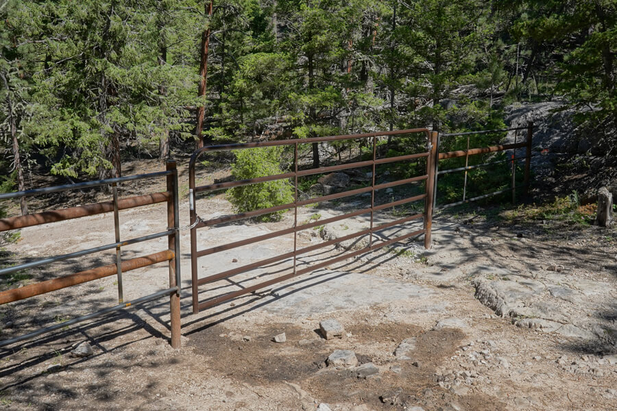 a metal gate across a dirt road locked by a chain with a forest background