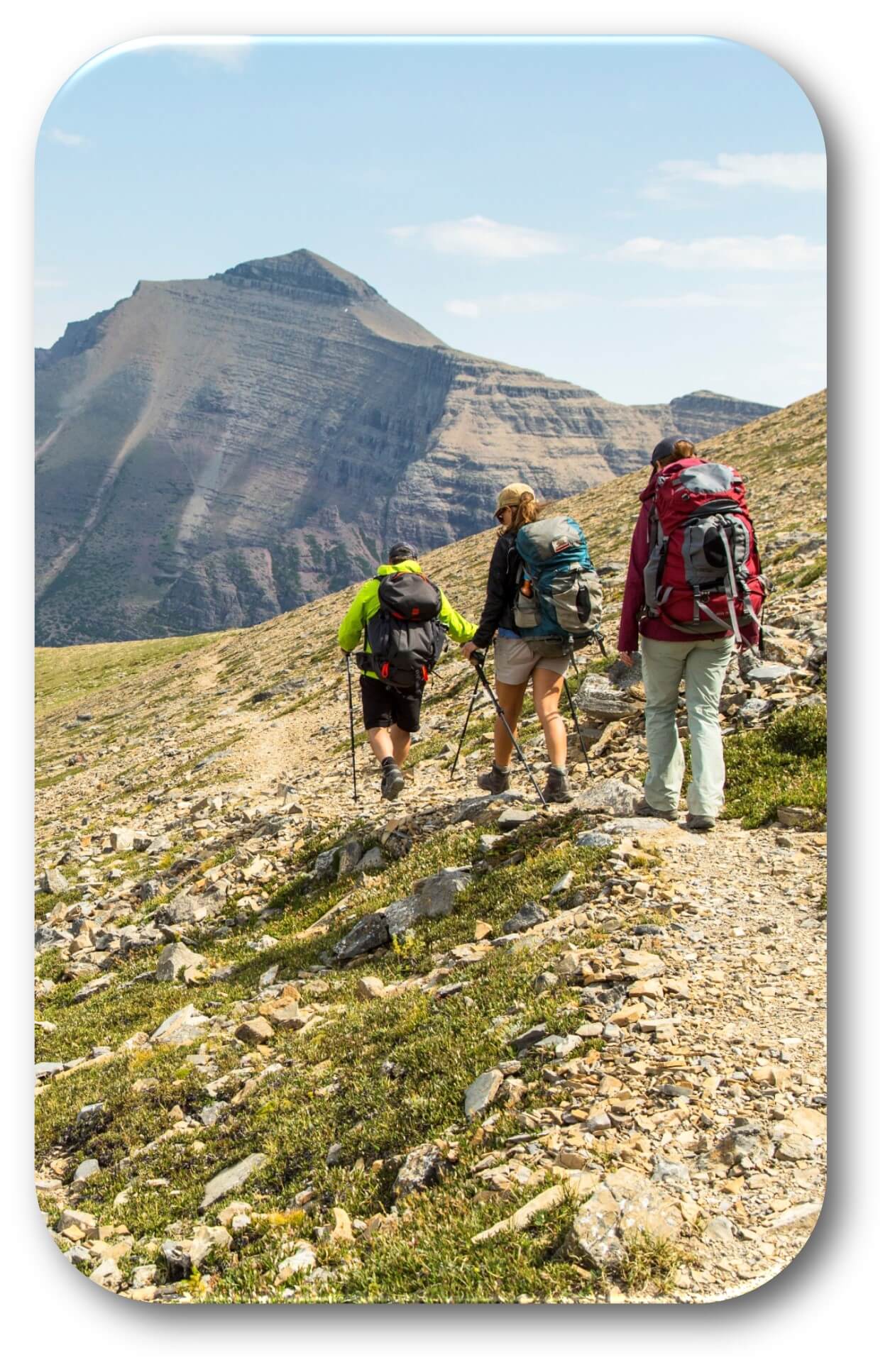 Three hikers walking on a rocky trail with a rocky mountain in the background